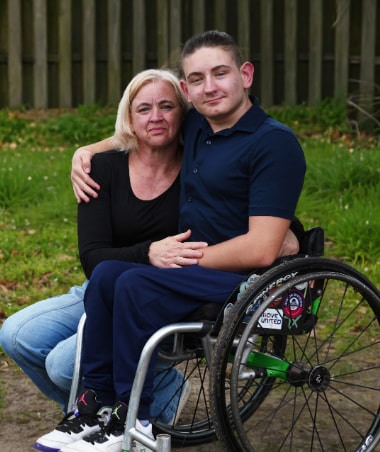 A mother hugged by her son who is sitting in a wheelchair outdoors