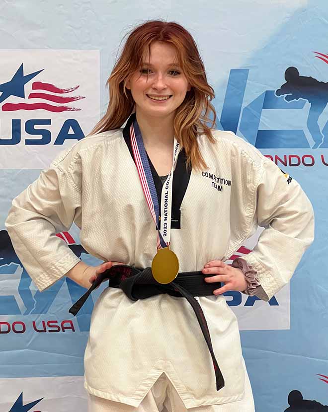 Image of Emma G, a junior at Great River Connections Academy, winning a medal at a Taekwando competition wearing her karate gi. 