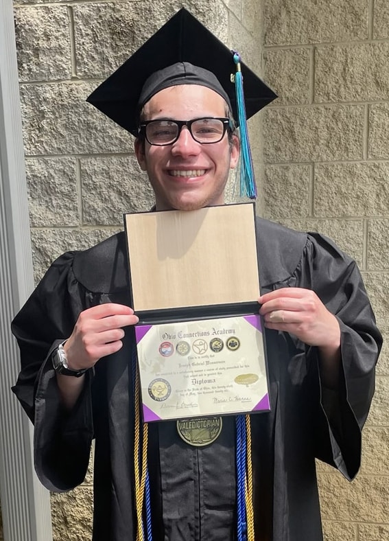 Joseph wearing a cap and gown and holding up his Ohio Connections Academy high school diploma