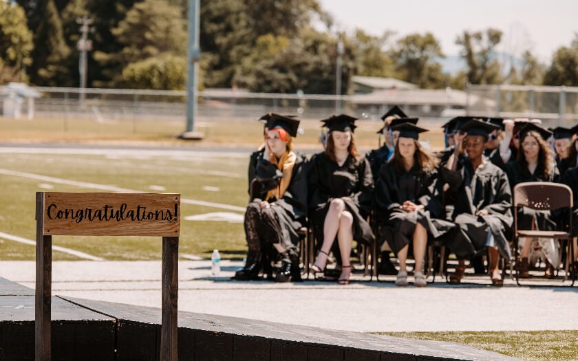 WillCA students sit waiting for their diplomas behind a congratuations sign