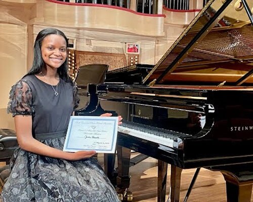 Image of Jada with her award. She is sitting next to a grand piano. 