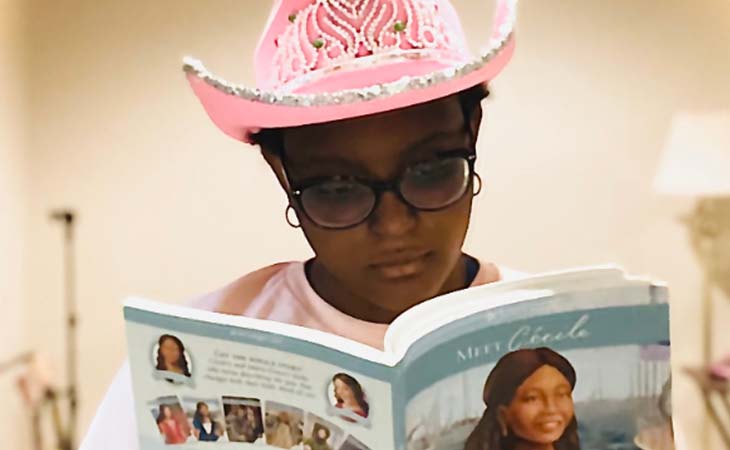 Caryn from Wisconsin Connections Academy reading a book wearing a pink hat.