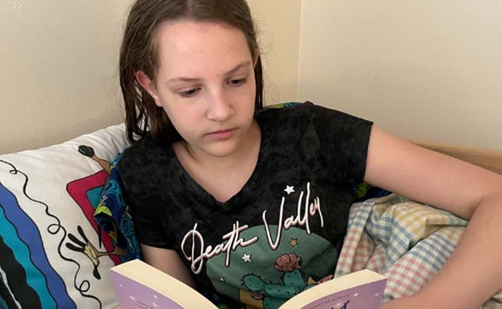 Liliana from Wisconsin Connections Academy reading a book while sitting in her bed.