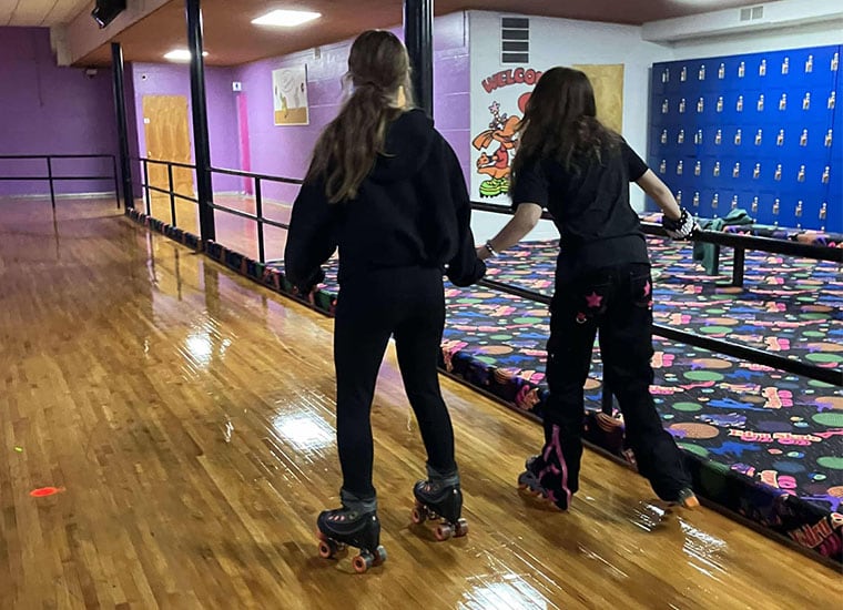 Two students help each other on the roller rink