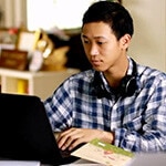 A high school student wearing headphones around his neck and typing on the computer