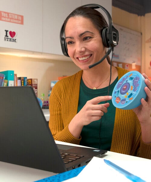 Teacher holding up a model while teaching in front of a computer