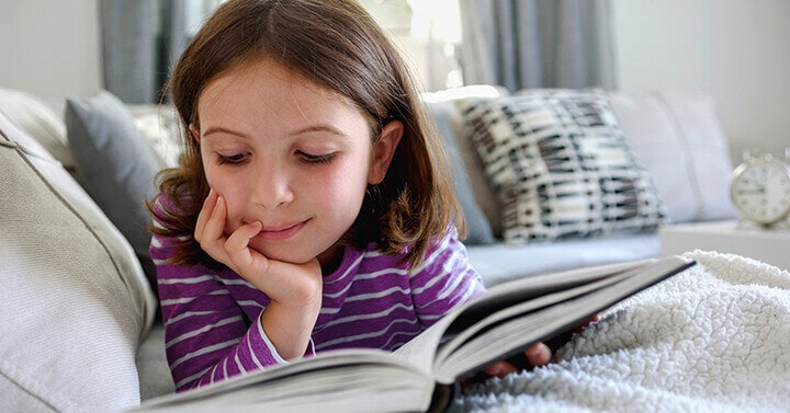 Young female student reading a book on her bed - Connections Academy 