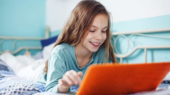 Girl laying on her bed looking at an orange laptop