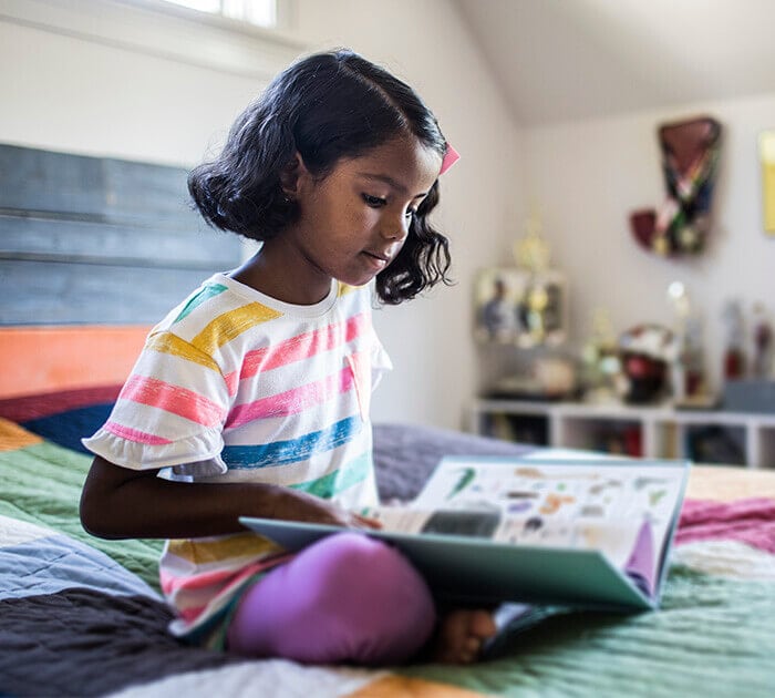 Elementary student reading a book in bed - Connections Academy