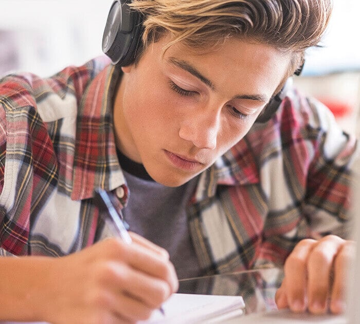 Teen boy concentrating on homework while listening to headphones