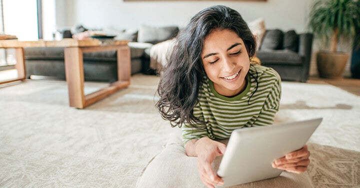 Girl reading a tablet while laying on the floor - Connections Academy