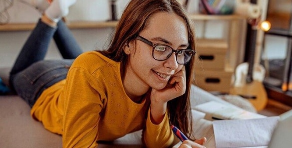 Connections Academy Student wearing a yellow shirt taking notes on her notebook in her room