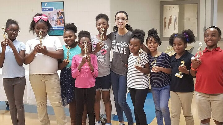 Madison is taking a photo with a group of students holding trophies