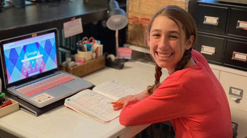 Maddie sitting at her desk with her notebook and laptop open