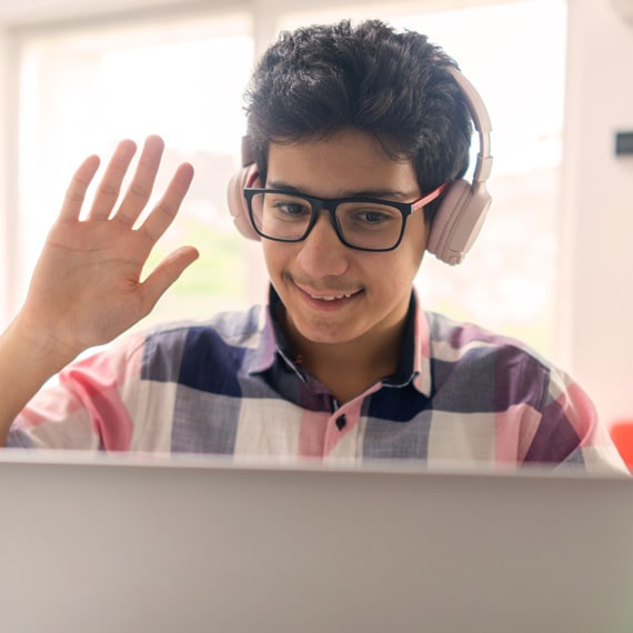 A boy wearing glasses is waving during his online class