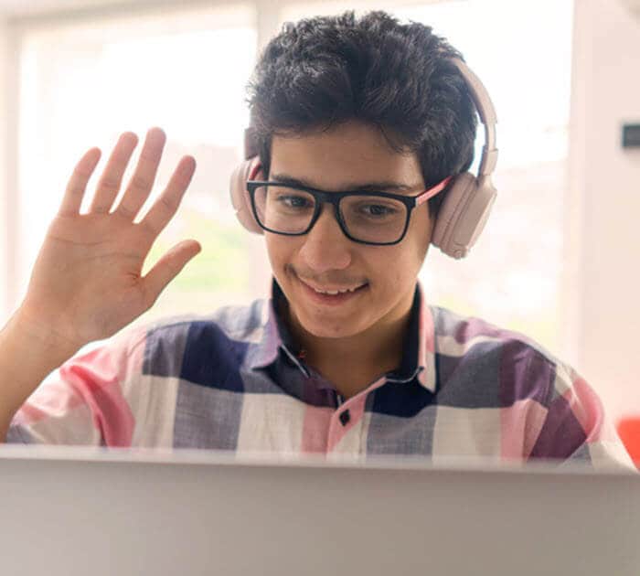 A middle school student waving to his classmates during an online class