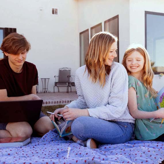 Family of three sitting on a blanket outside while learning - Connections Academy