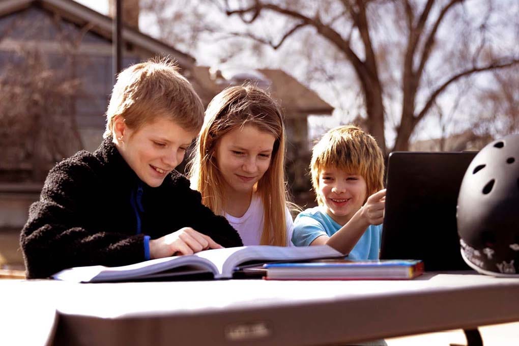 Three students sitting outside at a table studying on a laptop