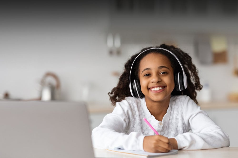 Ohio Connections Academy student in a white sweater looking at the camera smiling while taking an online class. 