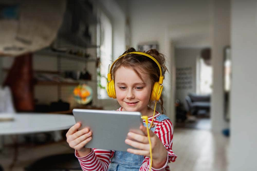 Young student in a red striped shirt and yellow headphones taking an online class at Michigan's Lighthouse Connections Academy. 