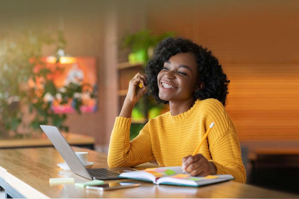 Young girl in a yellow sweater writing in a notebook while watching a lesson on a computer taking an online class at Virginia Connections Academy. 