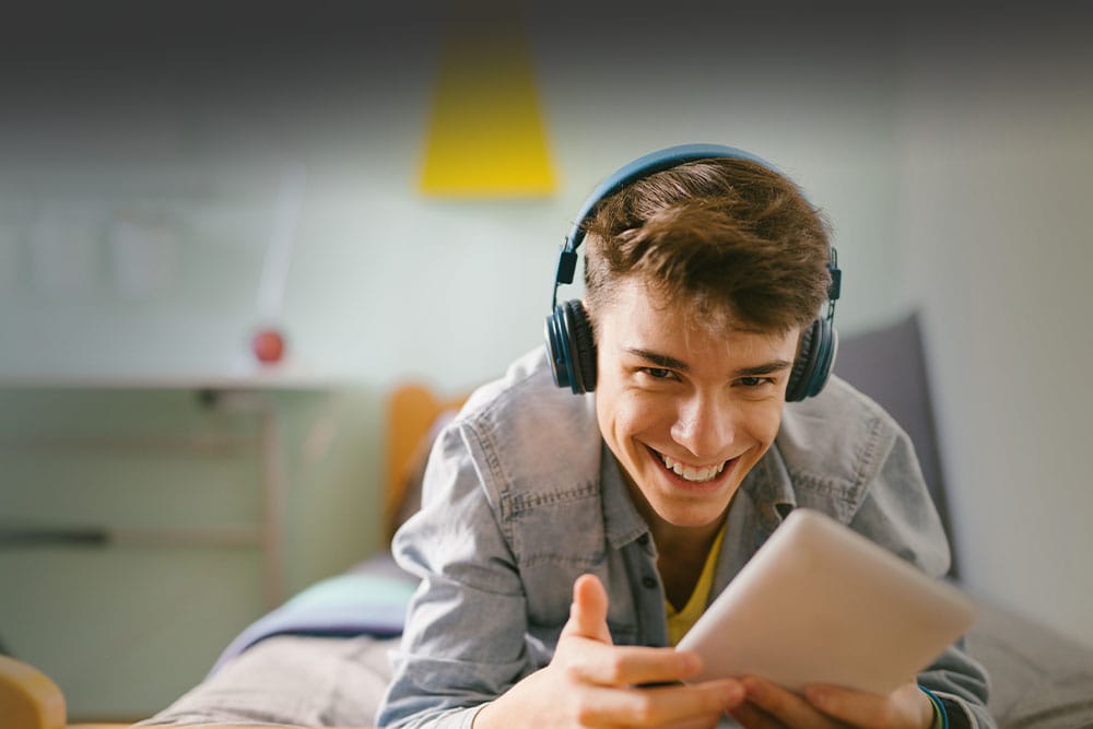 Young teen boy wearing headphones and looking at a tablet takign an online class for Wisconsin Connections Academy