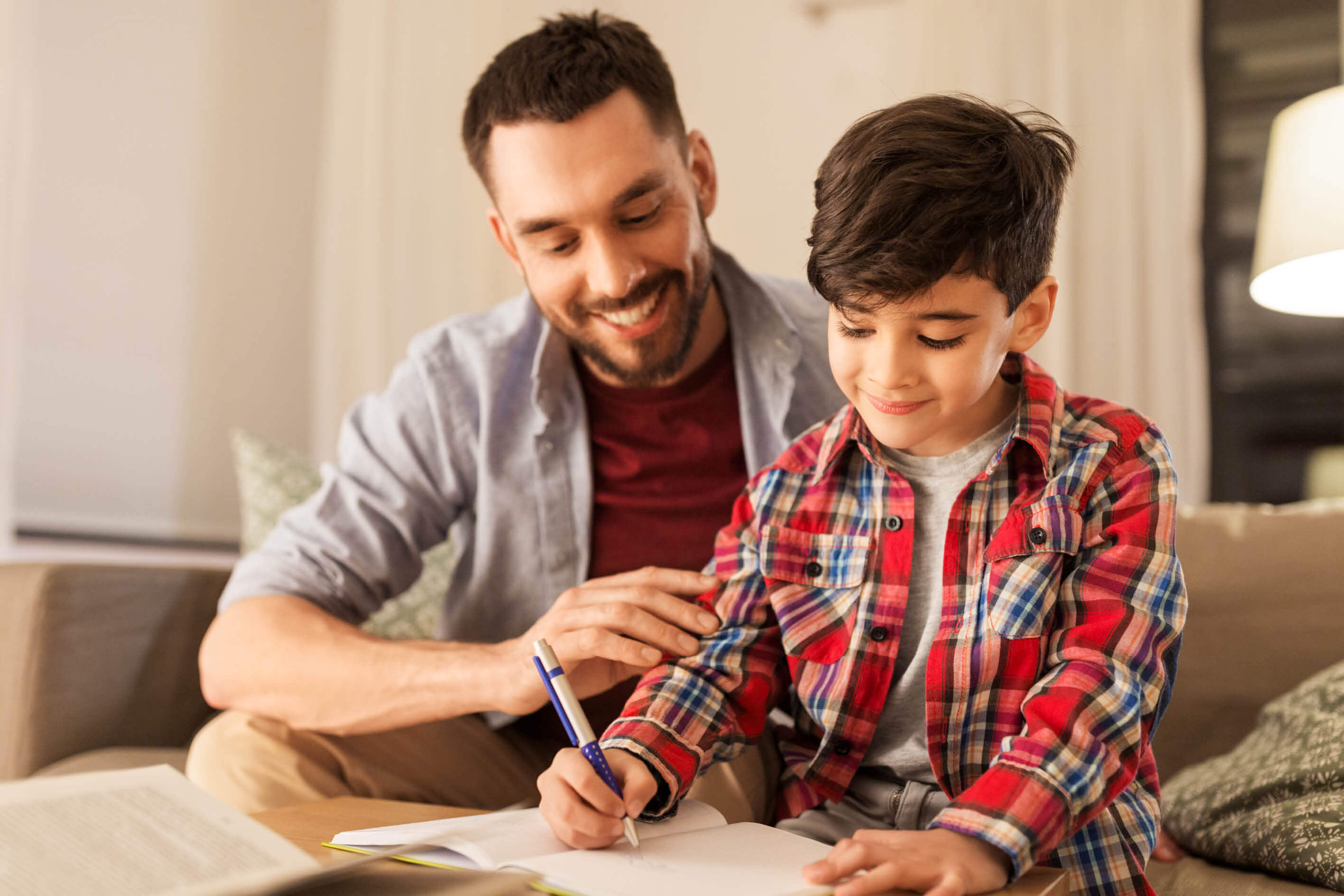Male parent and young boy holding pencil working together on an assigment