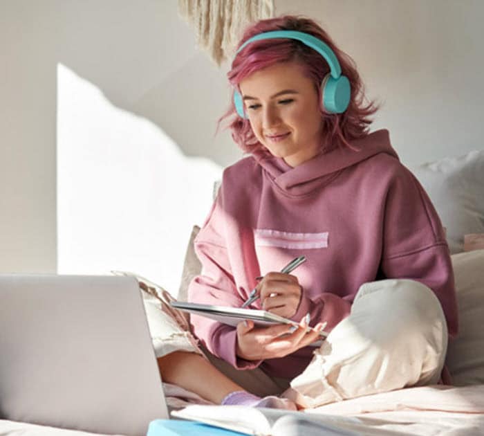 Teenage girl is sitting on her bed taking notes from her online lesson - Connections Academy