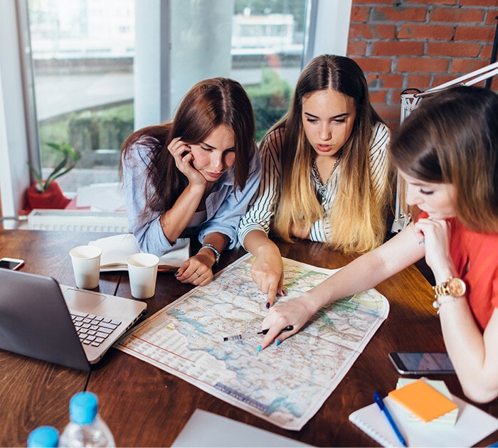 Family of three sitting at a table pointing at a location on a map - Connections Academy