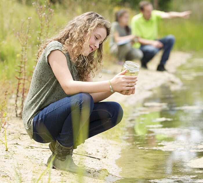 Femaile high school student on the edge of the water looking at a glass jar doing a sciece experiment at Connections Academy 