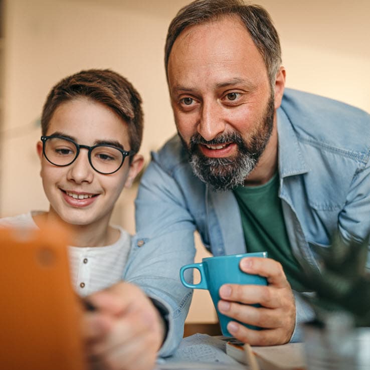 A father is pointing at a tablet with his son during an online class