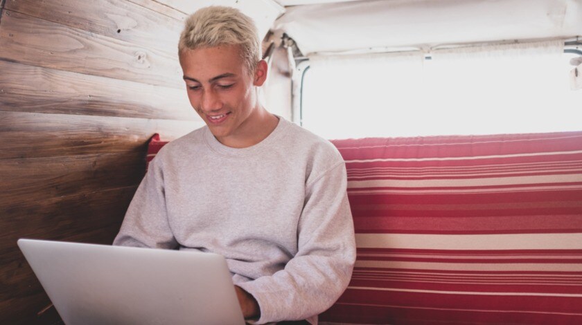 A teenage boy is looking at a laptop