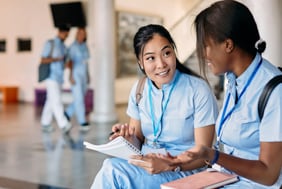 Two nursing students engaged in a conversation and wearing scrubs