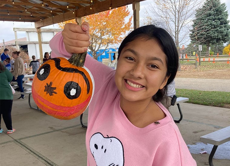 A student smiling holding a painted pumpkin