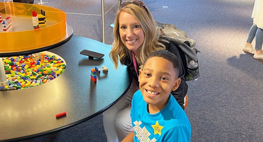A teacher and student sitting at the Lego building area and smiling.