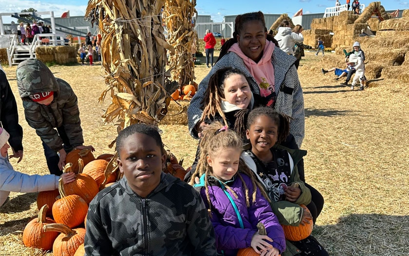 Students and an adult sitting on stacks of hay and holding pumpkins