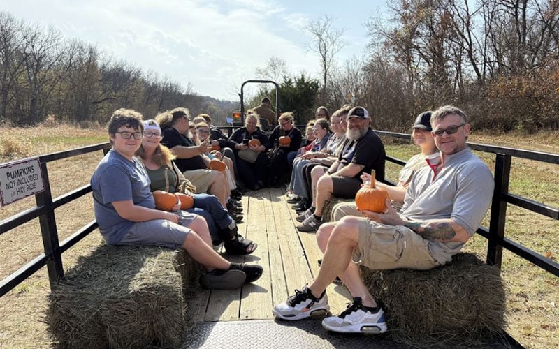 A group of students and their families holding pumpkins on a hayride at Weston Red Barn Farm