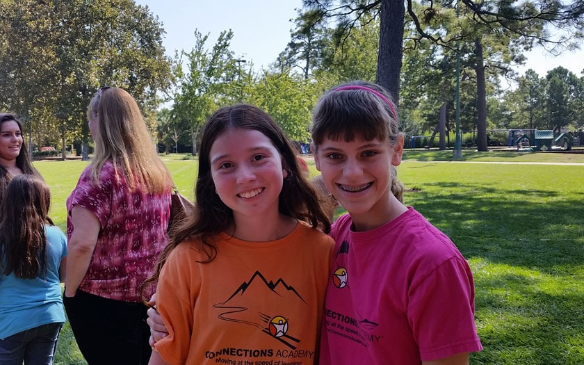 Two girls at a park are standing next to each other smiling