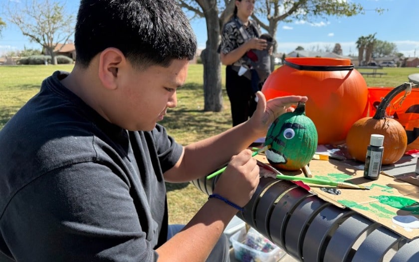 A student paints a pumpkin while sitting at a park table