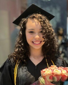 Juliah smiling in her graduation gown while holding flowers