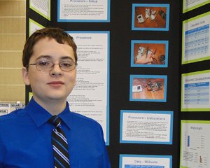 Matthew standing into a posterboard presentation in wearing a blue shirt and tie