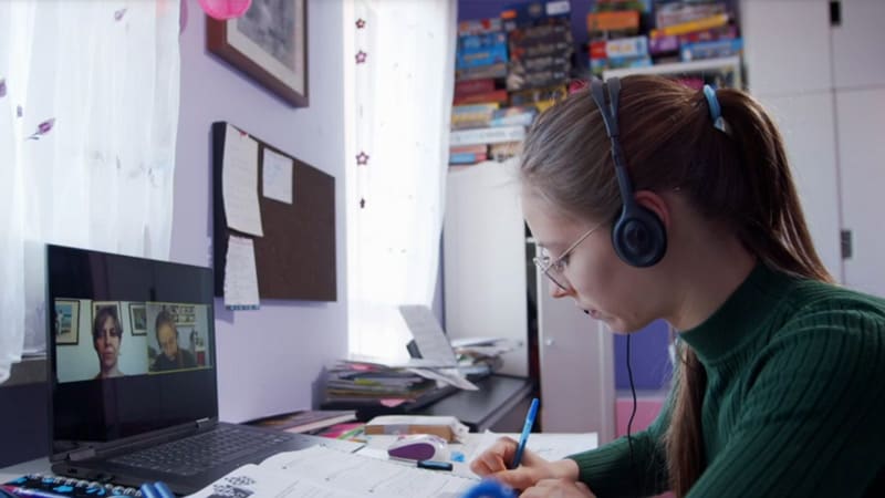 A student sitting at a desk and attending a live online school lesson