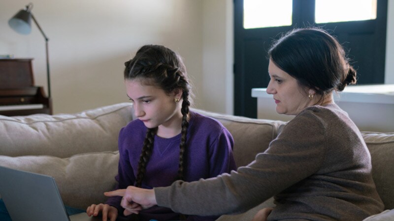 Connections Academy student, Ella, sitting on a couch with her Learning Coach, engaging in online school work on laptop
