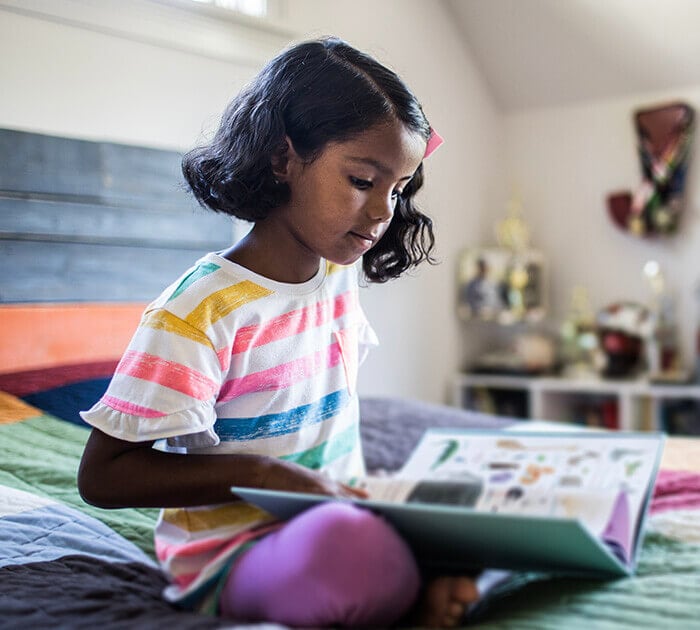 A young girl is sitting on a bed reading a book