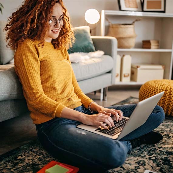 A high school student in a yellow sweater sitting down with a laptop