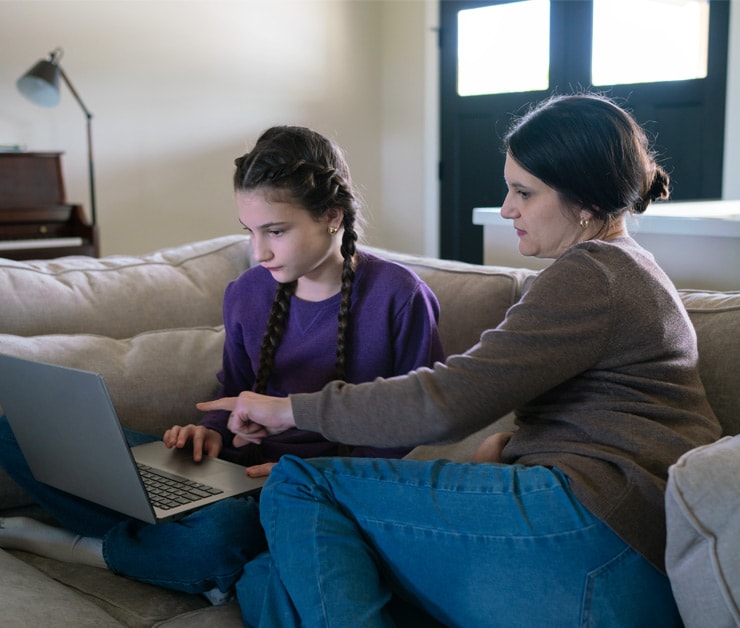 Connections Academy student, Ella, sitting on a couch with her Learning Coach, engaging in online school work on laptop