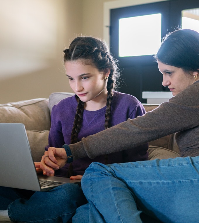Connections Academy student, Ella, sitting on a couch with her Learning Coach, engaging in online school work on laptop