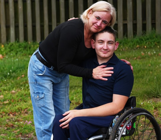 Connections Academy student, Ryan, sitting in a wheelchair while his mom bends down to embrace him