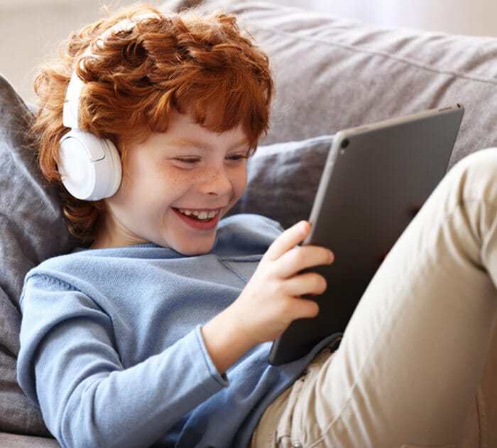 A young boy listening to headphones and smiling at his tablet