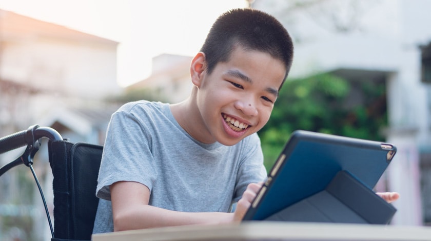 Online school student sitting on couch, wearing headphones, writing in a notebook and using laptop